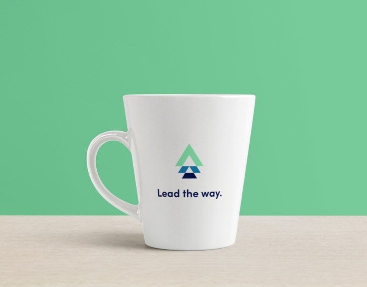 A white mug with an arrow logo that reads "lead the way" in front of a green background.