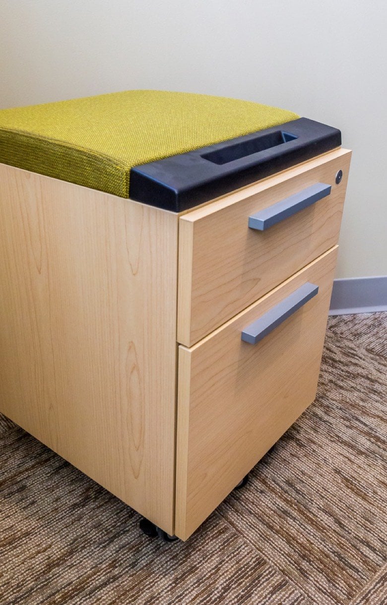 A wooden filing cabinet with a cushioned top.