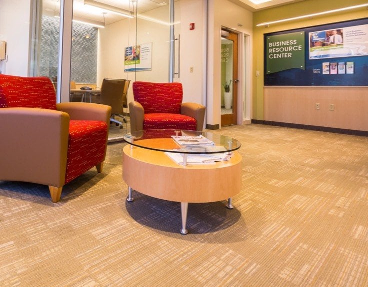 A waiting rom with a wooden table and two red and brown upholstered chairs.