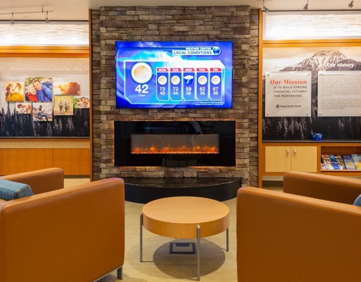 A waiting room with a television displaying the news above a fireplace.