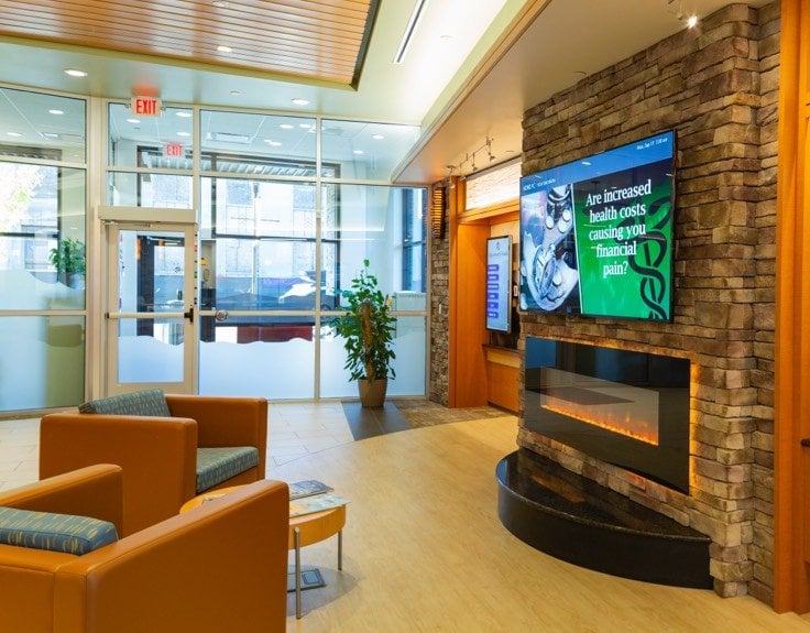 A waiting room with a television screen above a fireplace.