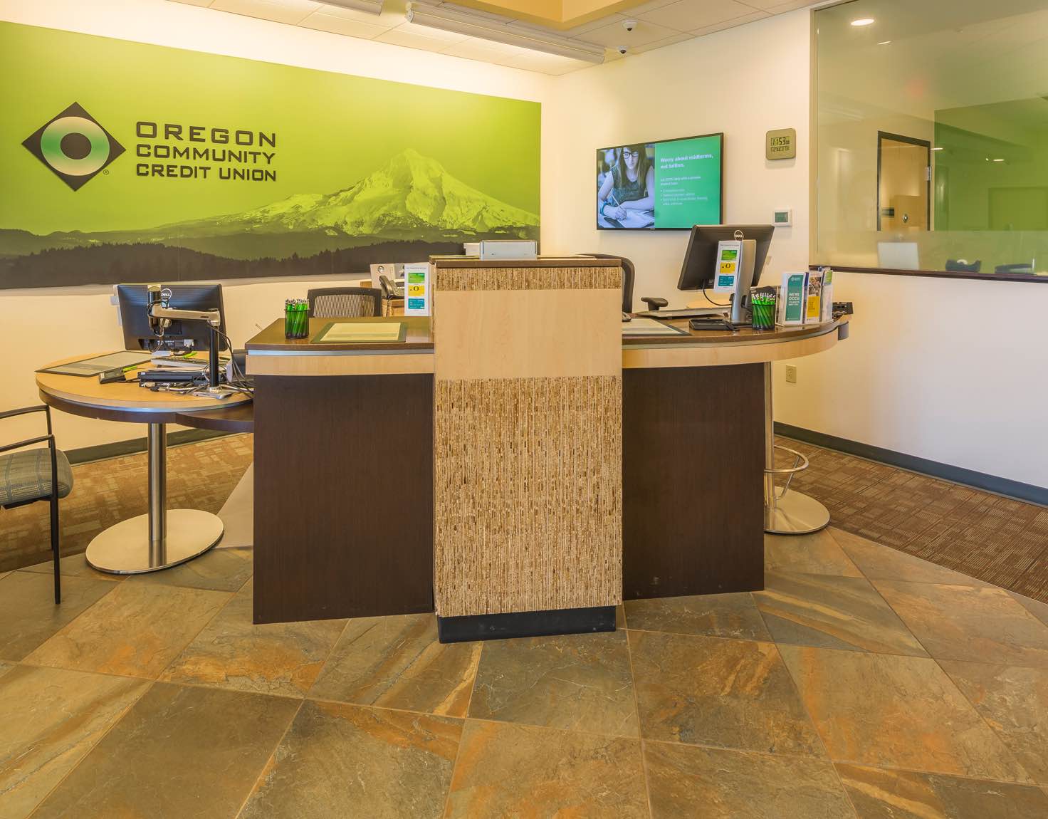 A wooden desk in a bank with a green sign behind it displaying a mountain range.