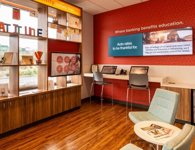 A cozy bank lobby featuring digital signage on the wall and a desk with a chair, creating a comfortable workspace.