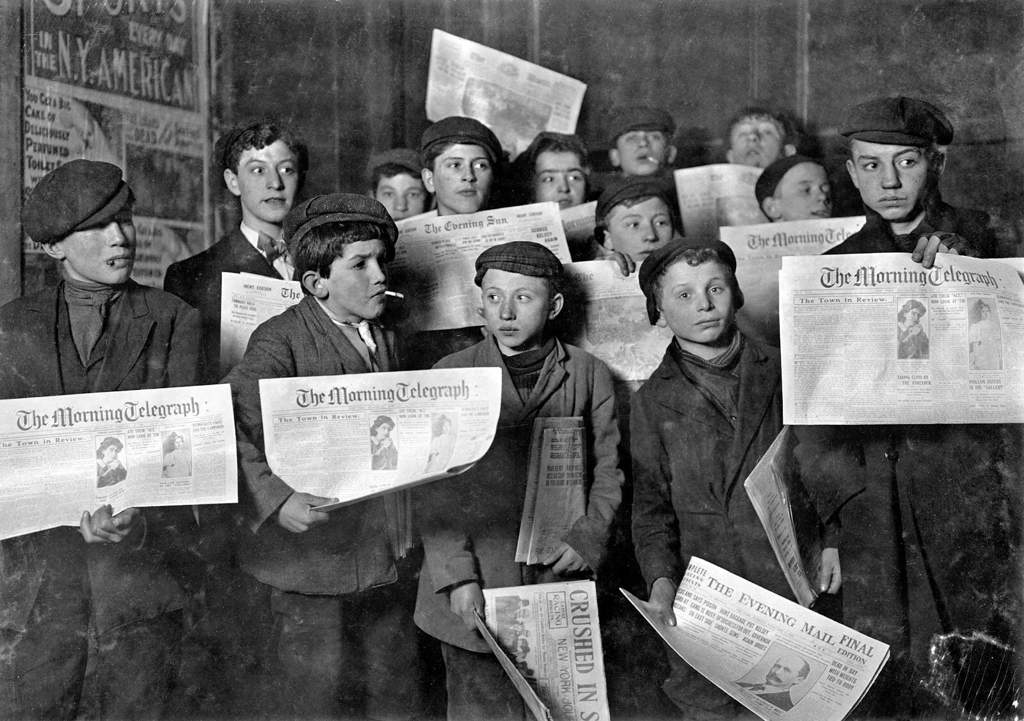 An old, black and white photo of young children holding newspapers.