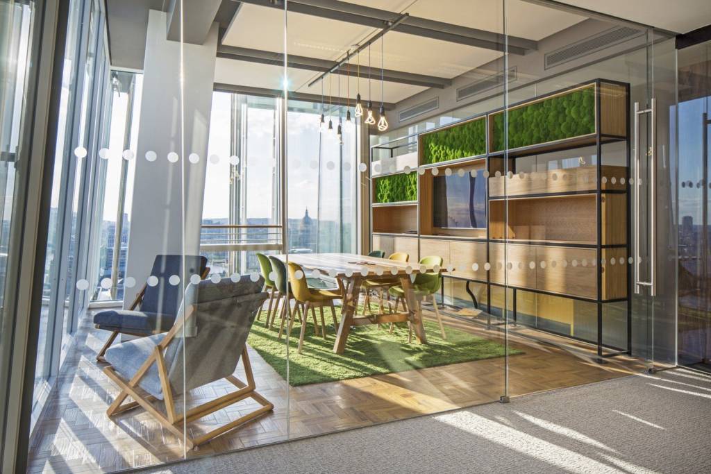 A glass conference room with a small wooden table and a wall of shelves.