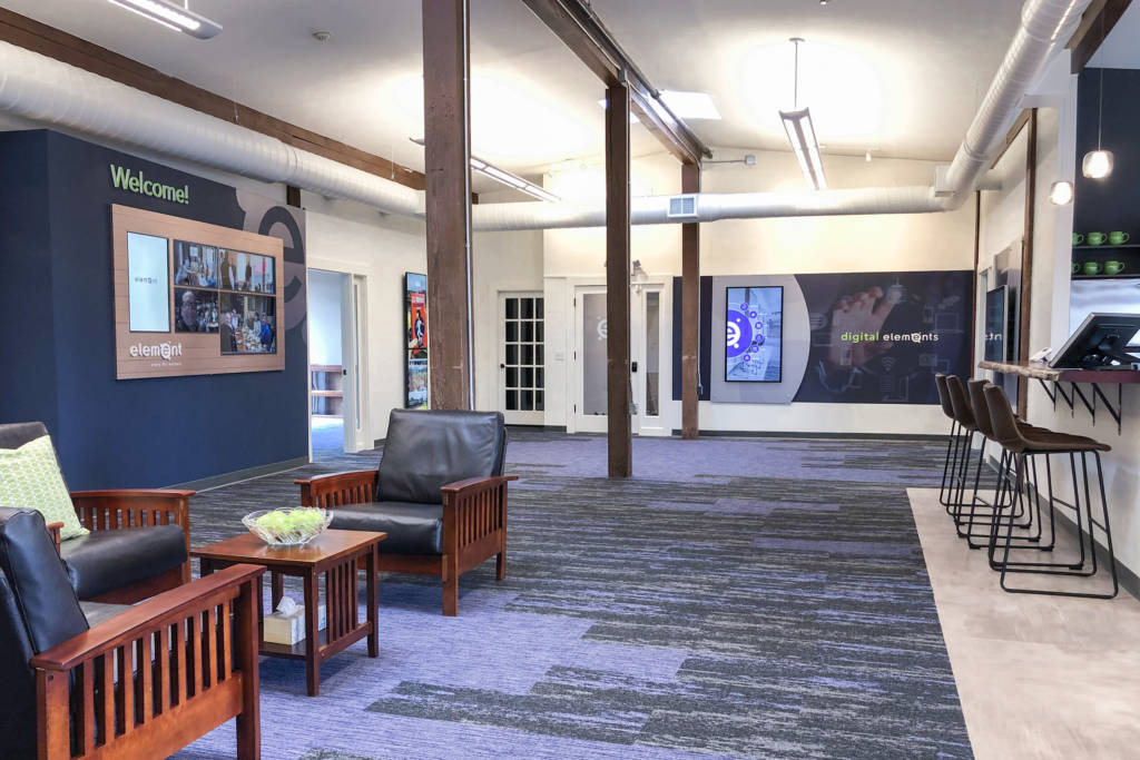 A waiting area with black leather chairs and a wall of screens.