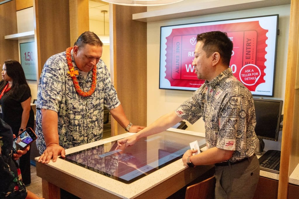 Two men in Hawaiian shirts using a tabletop touchscreen.