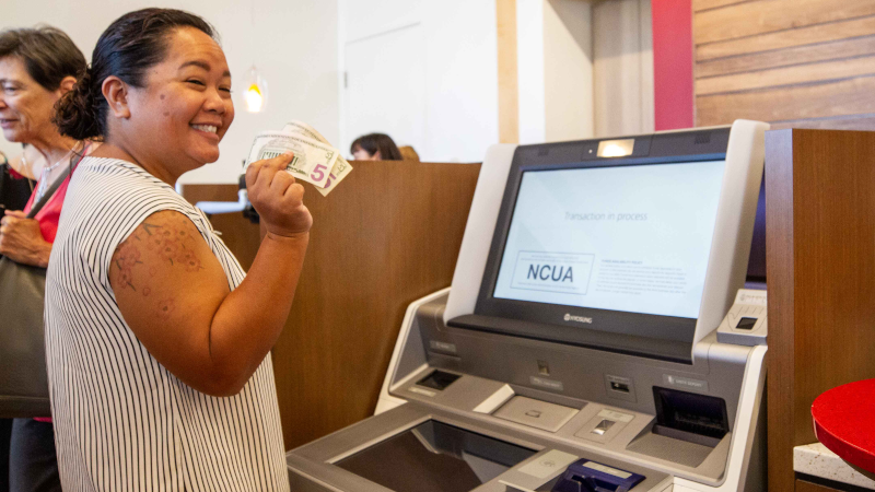 A woman holding cash, using a self-serve teller machine.