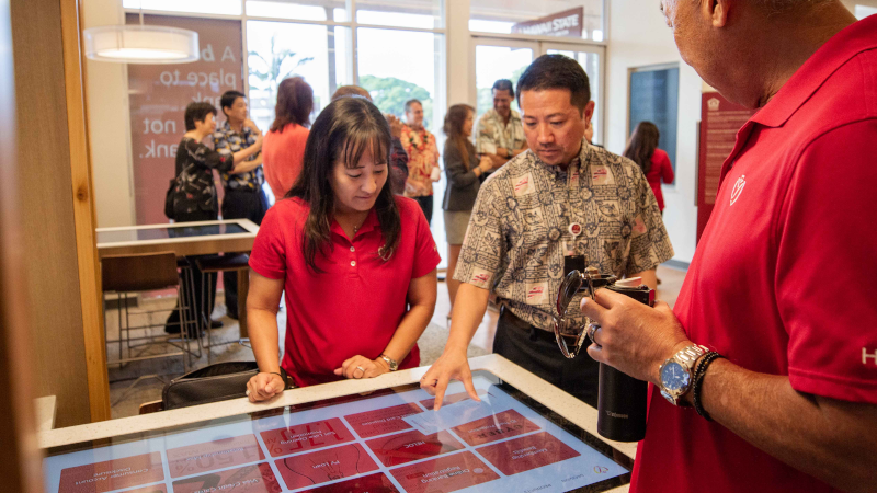 Three people standing over, and touching a table with a touchscreen top.