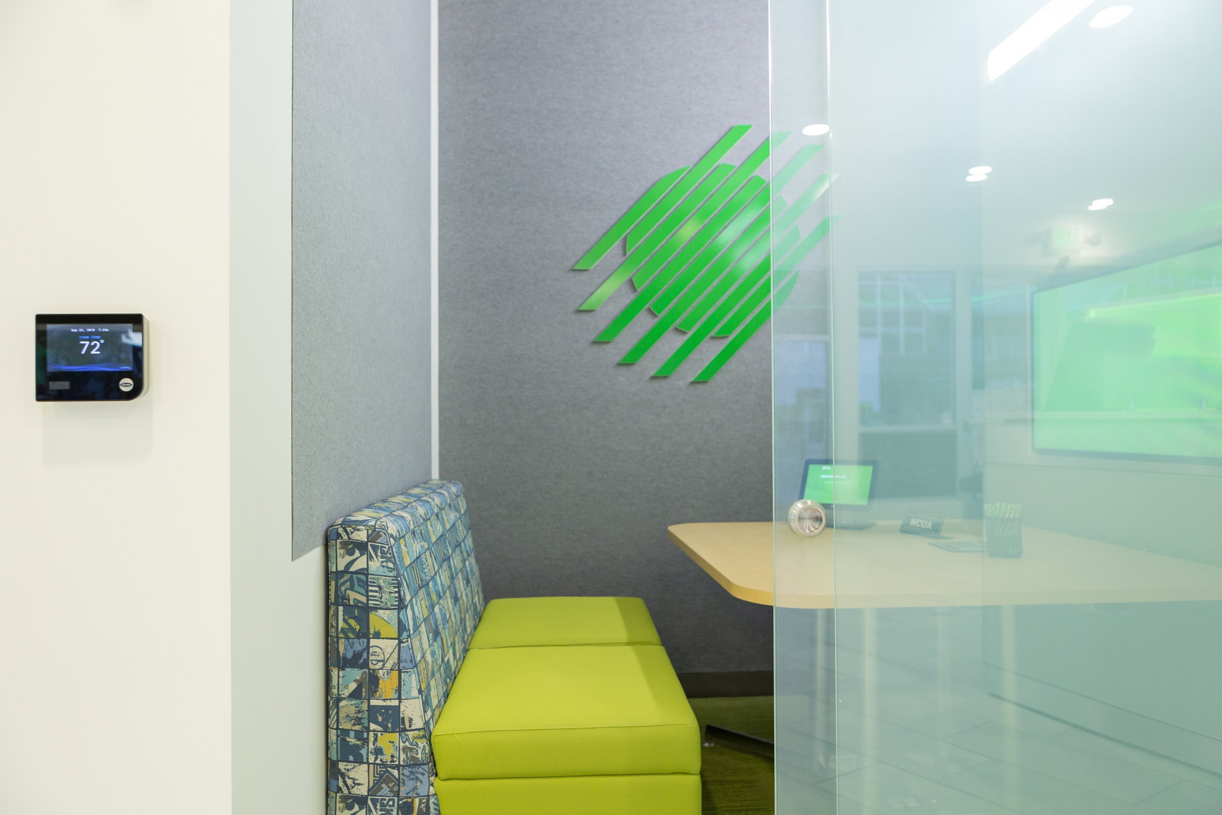 A green sofa in front of a wooden table, inside a small glass room.