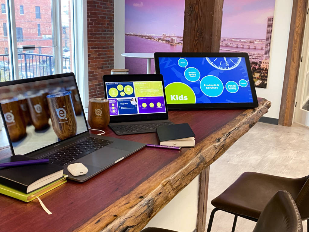 A laptop, ipad, tablet, airpods, books, and a mug, all on a desk.