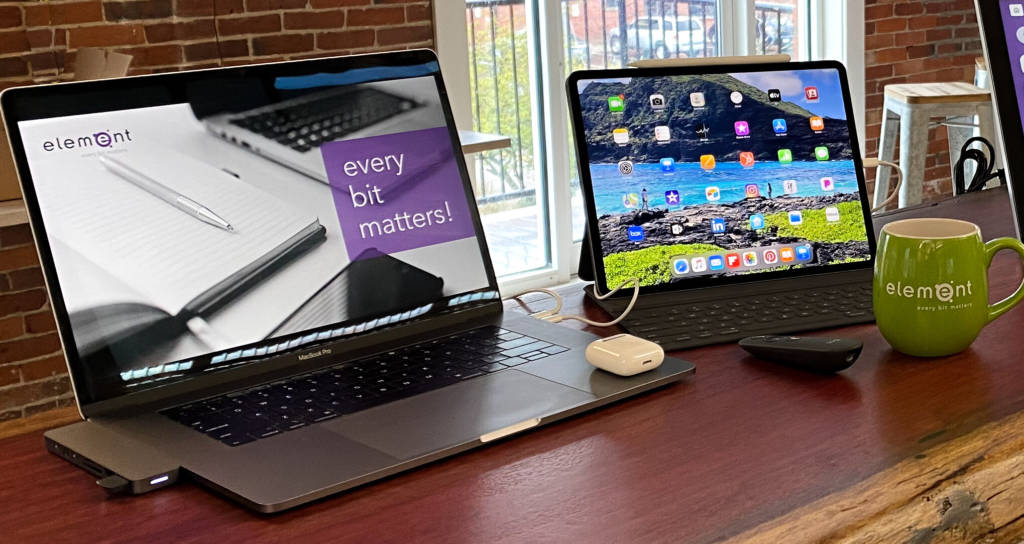 A laptop, ipad, airpods, and a mug, all on a desk.