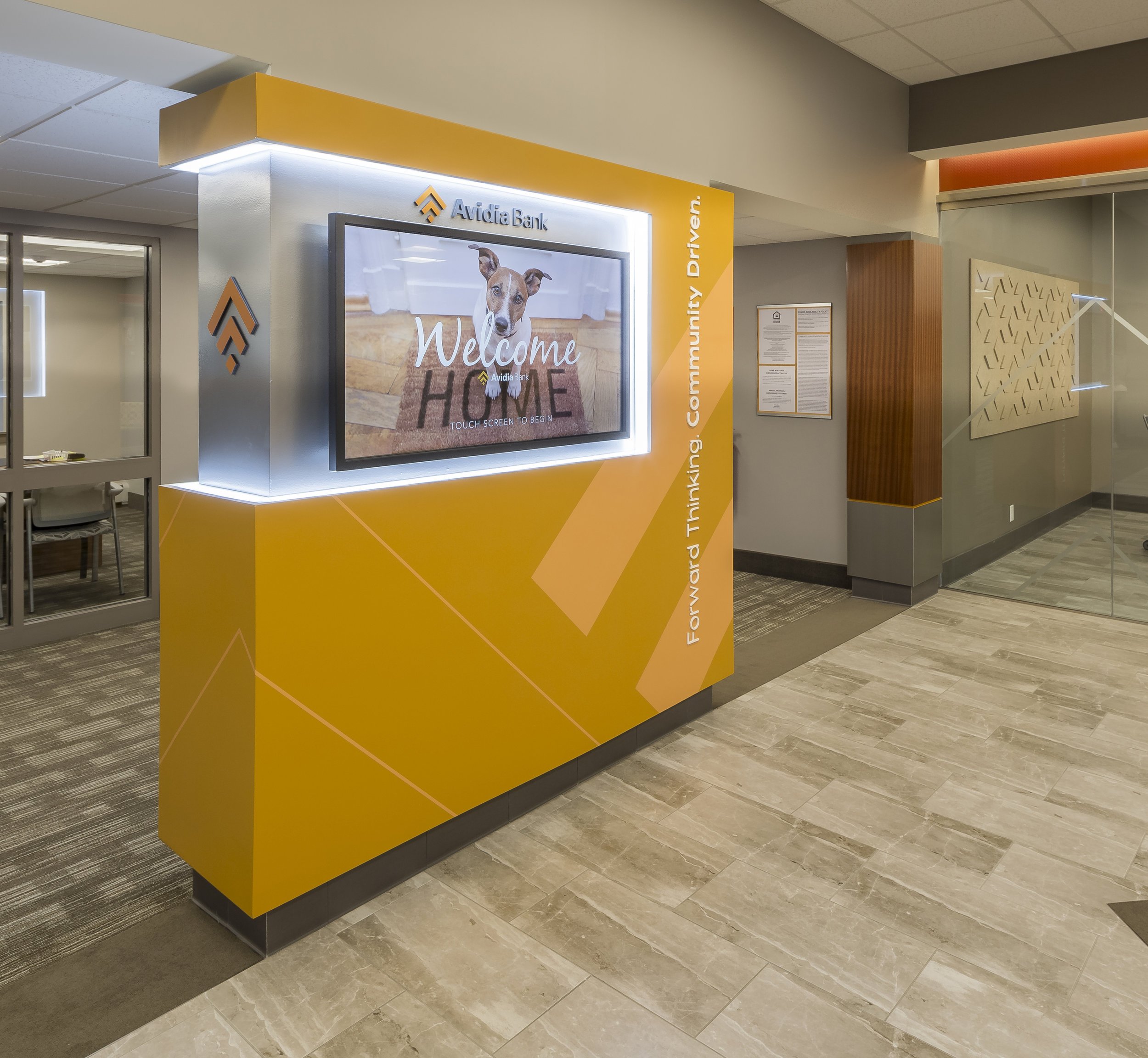 A lobby with an orange wall with a television screen hung on it.