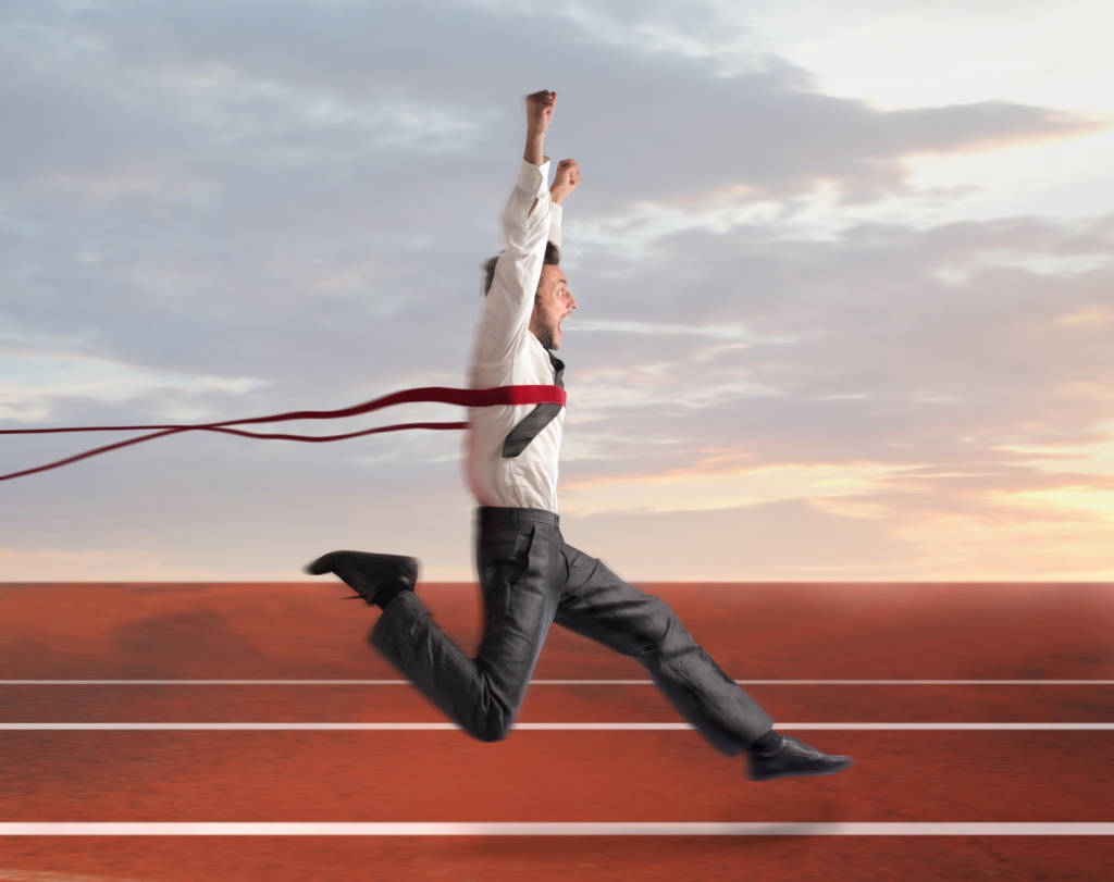 A man in a suit running through a finish line on a track.