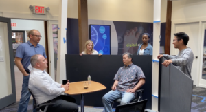 A group of coworkers standing and sitting in a circle talking.