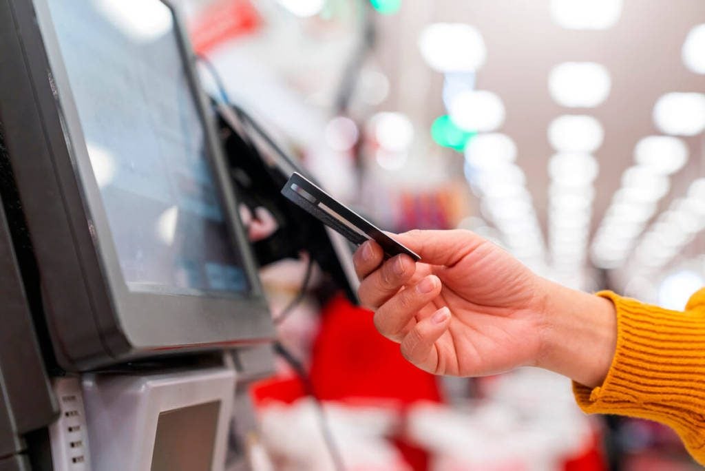 A person presenting a credit card at a checkout counter, ready to complete a purchase.