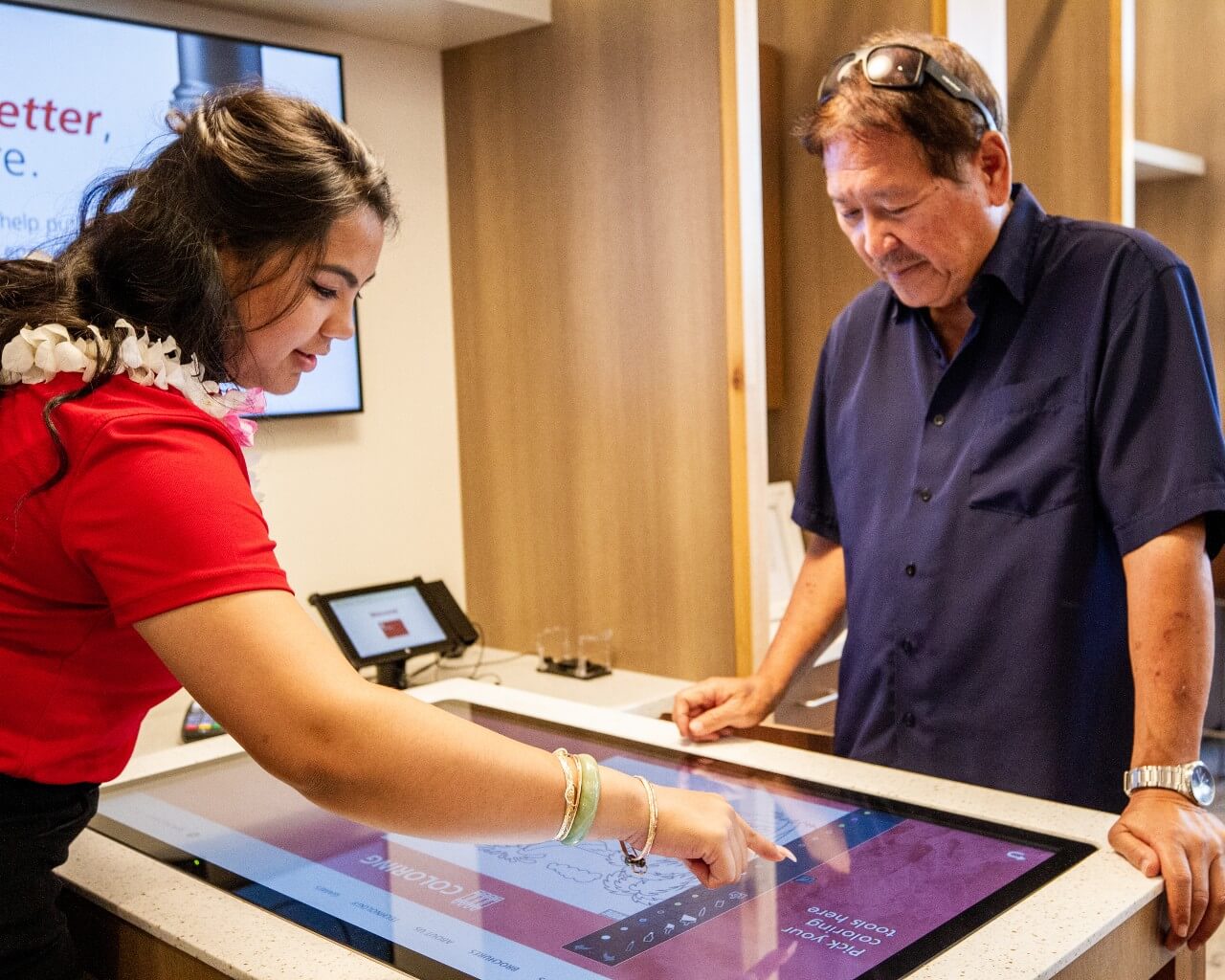 A credit union representative assists a man at a digital information kiosk, showcasing personalized assistance in the banking customer experience.