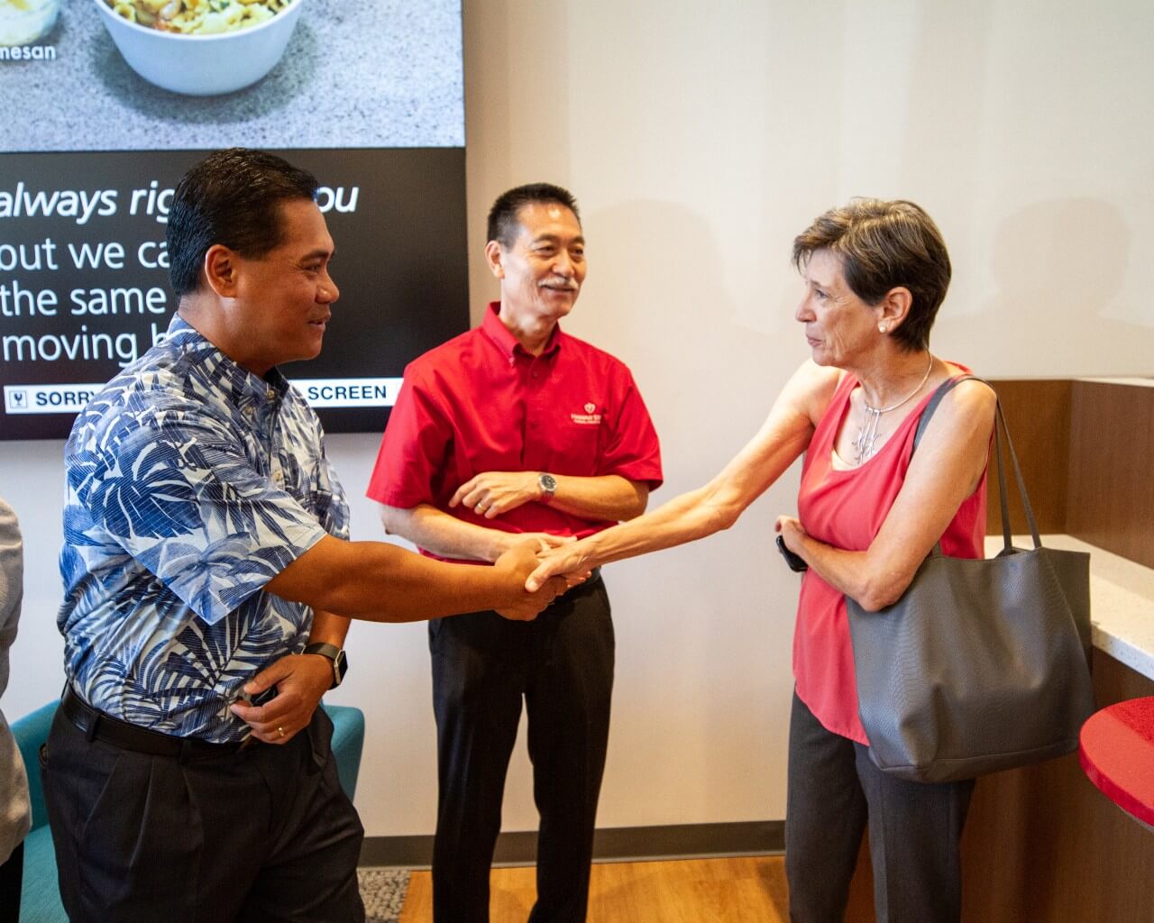A man shakes hands with a woman as another man stands between them, illustrating a personal greeting as part of a welcoming banking customer experience.
