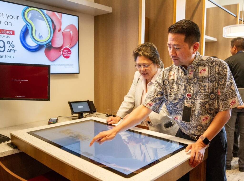 A credit union employee assists a woman with a digital interactive display, highlighting a supportive banking customer experience.
