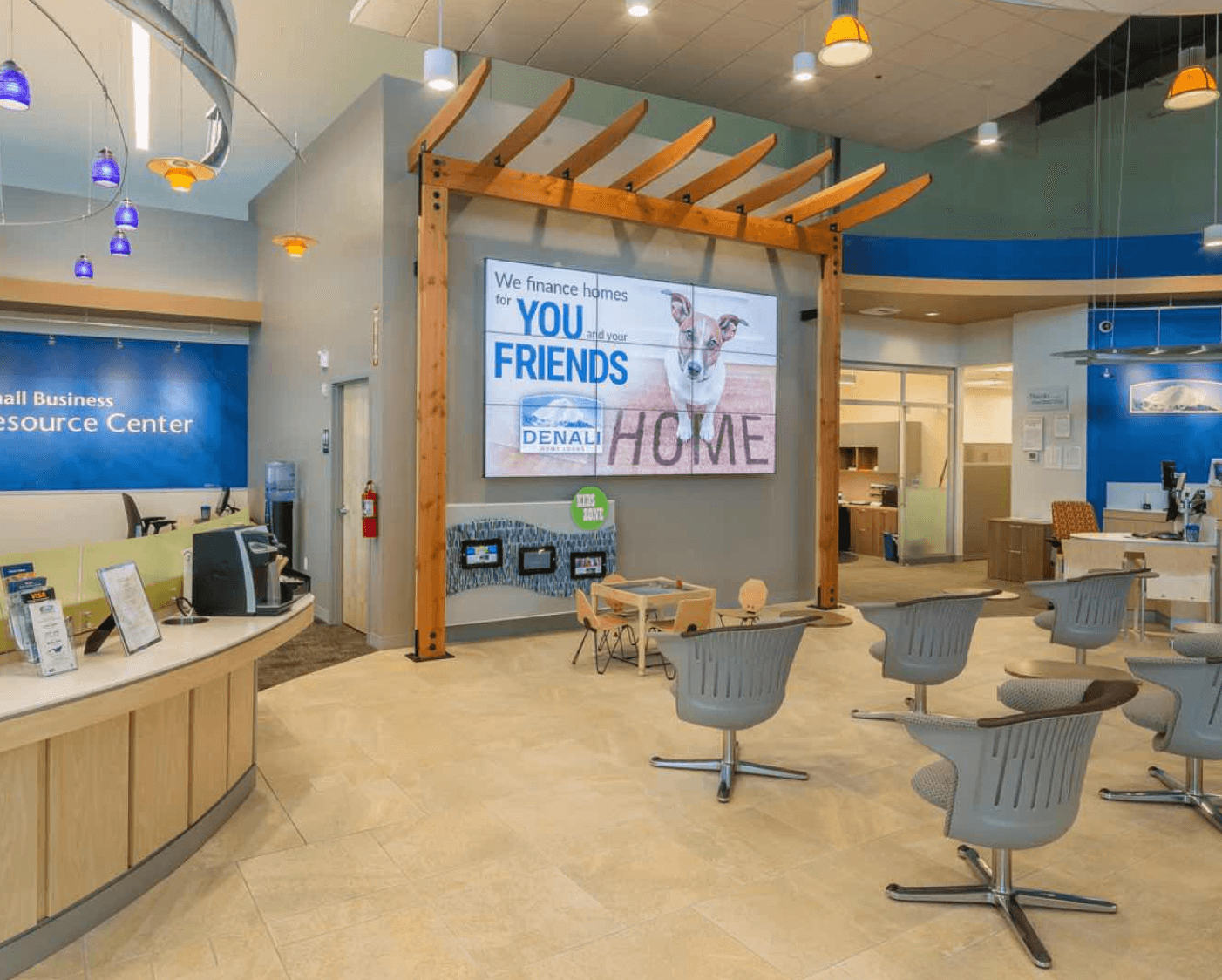 A welcoming financial branch lobby featuring a large central digital display promoting home financing, with comfortable seating and contemporary design elements.