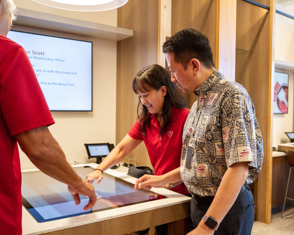 Three people looking at a touch screen in a desk