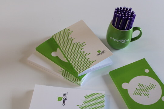 desk filled with element group merchandise such as green notepads and purple mug.